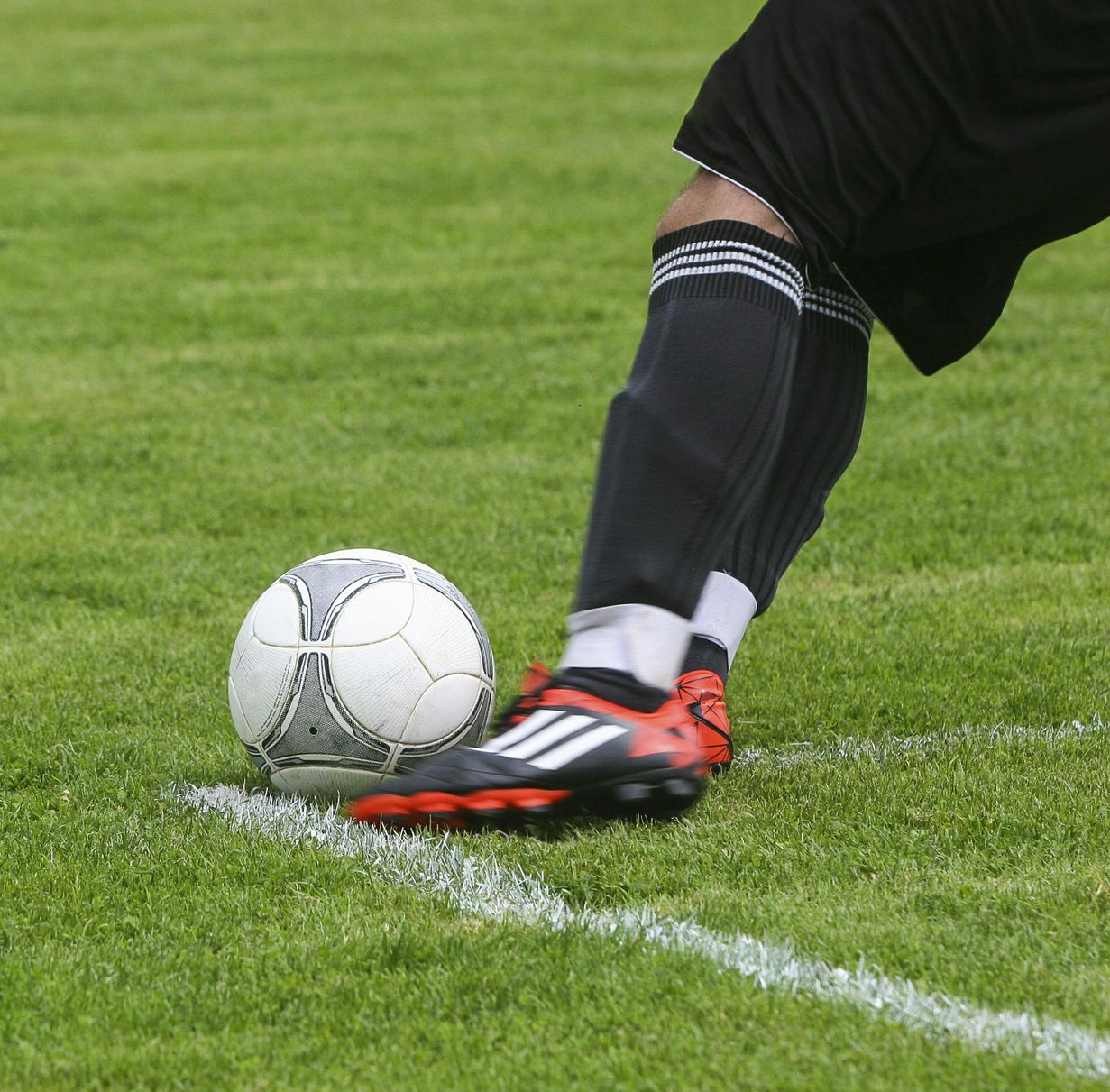 Soccer player’s foot in red cleat poised by a white ball on the sideline line