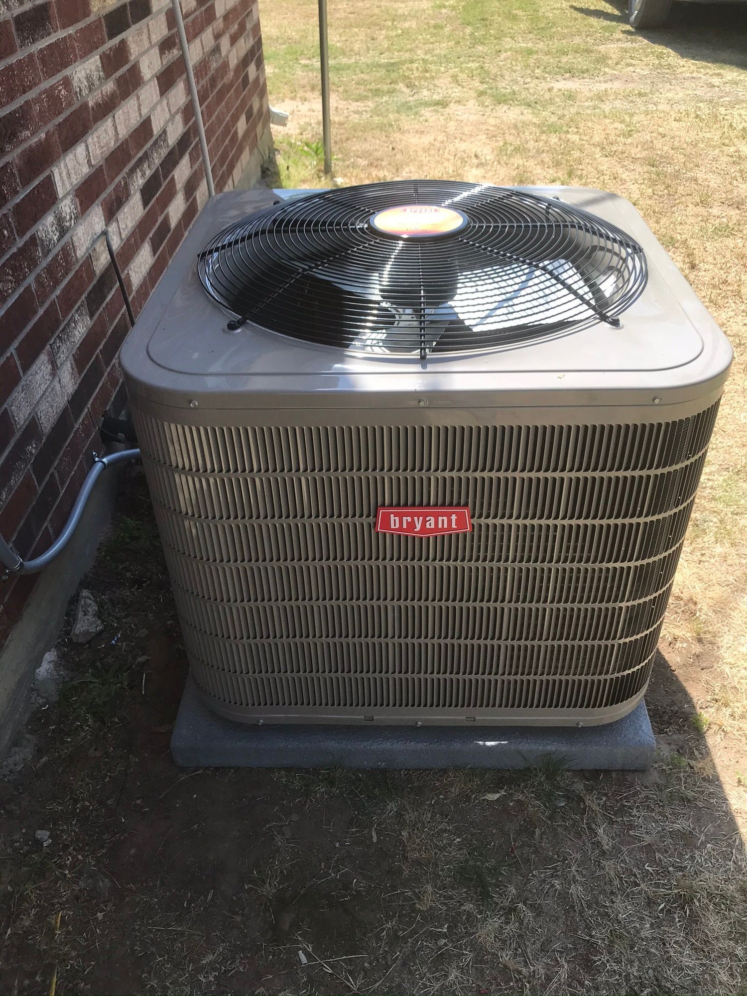 A large air conditioner is sitting outside of a brick building.