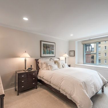 A bedroom with a bed , dresser , lamp and window.