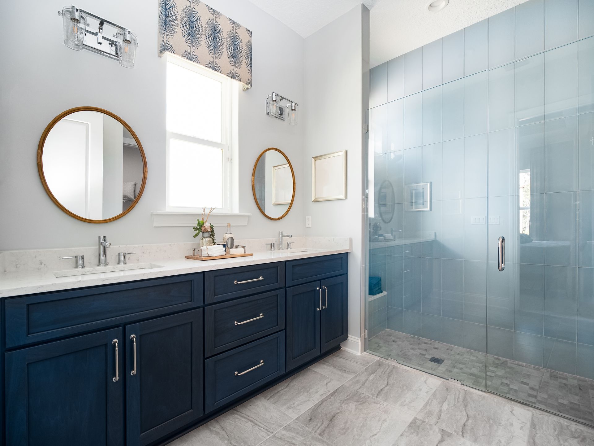 Bathroom with blue vanity, gold mirrors, light blue shower, and window with patterned valance.