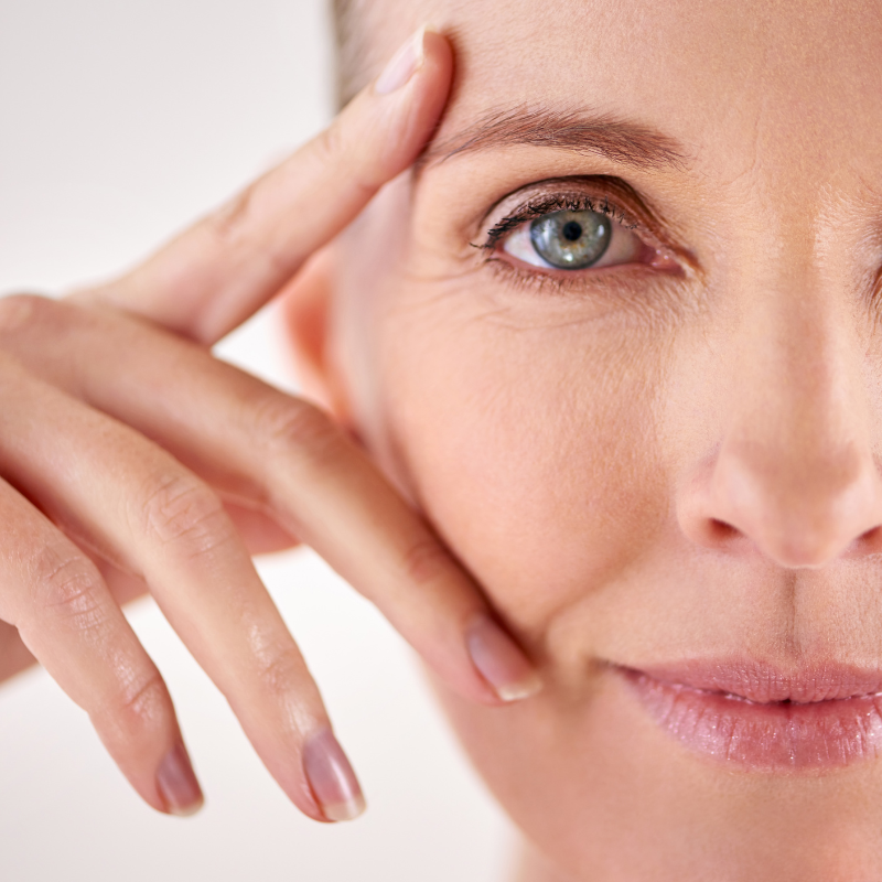 Woman's face close-up, touching her eye and forehead with fingers; wrinkles are visible.