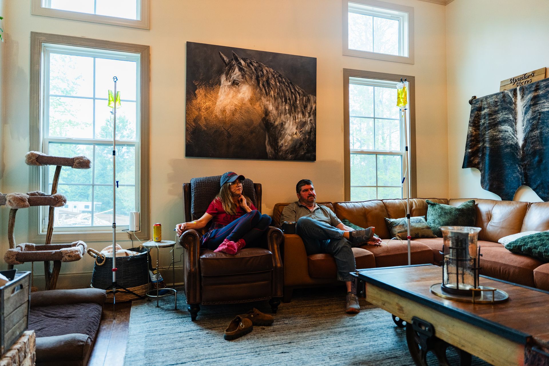 Man on sofa with IV drip, talking on phone, using laptop, in a living room.