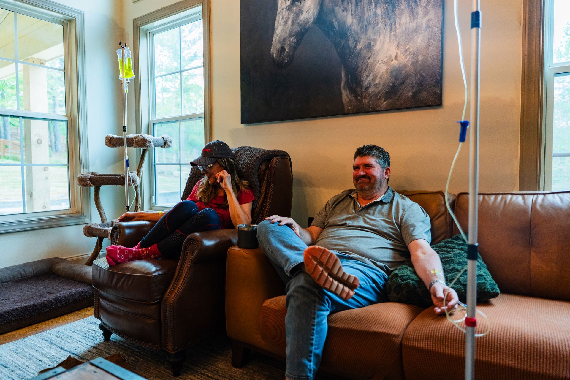 Man on sofa with IV drip, talking on phone, using laptop, in a living room.