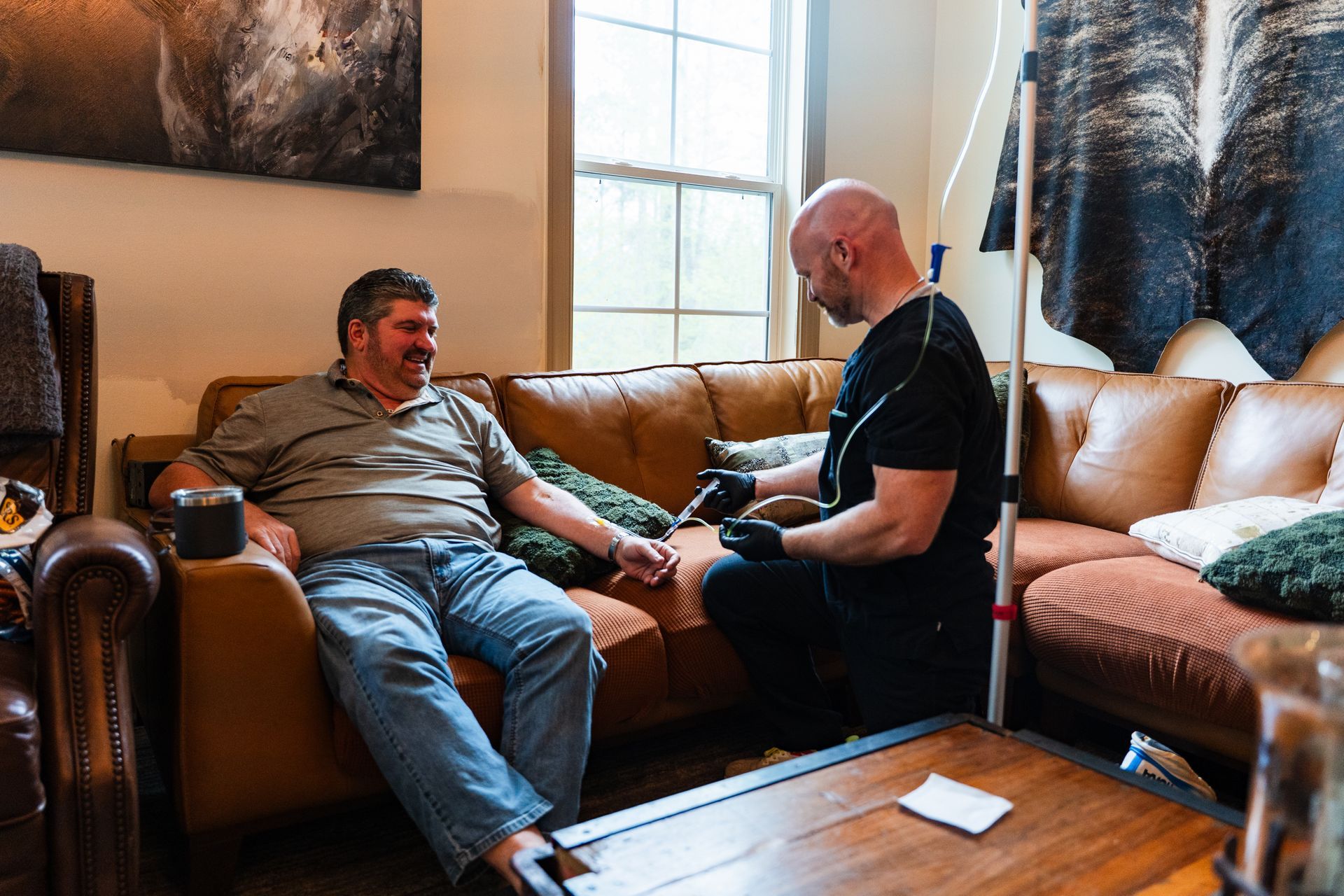 Man on sofa with IV drip, talking on phone, using laptop, in a living room.