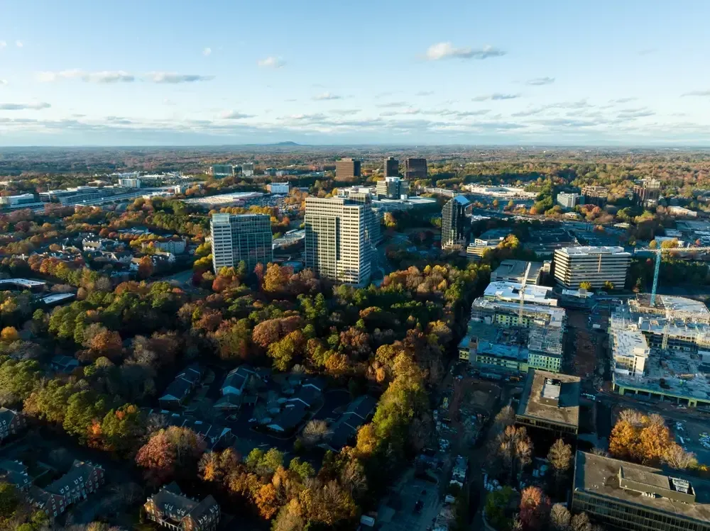 Aerial view of buildings and autumn trees in a city, under a blue sky.