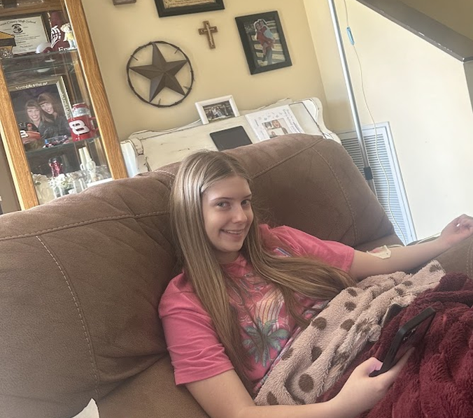 Blonde teen girl smiling on a brown couch, covered with a blanket, in a living room.