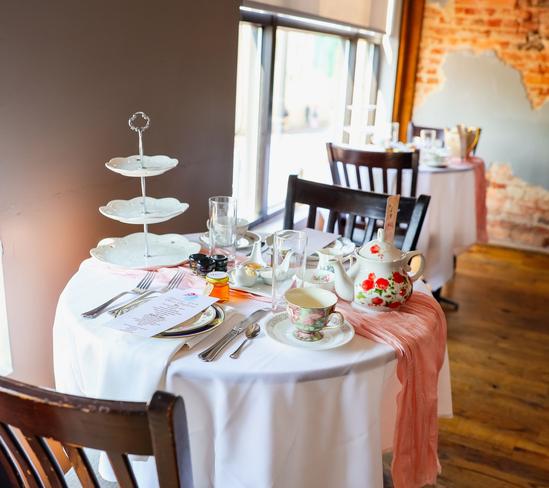 A table with plates , cups , glasses and a cake stand on it