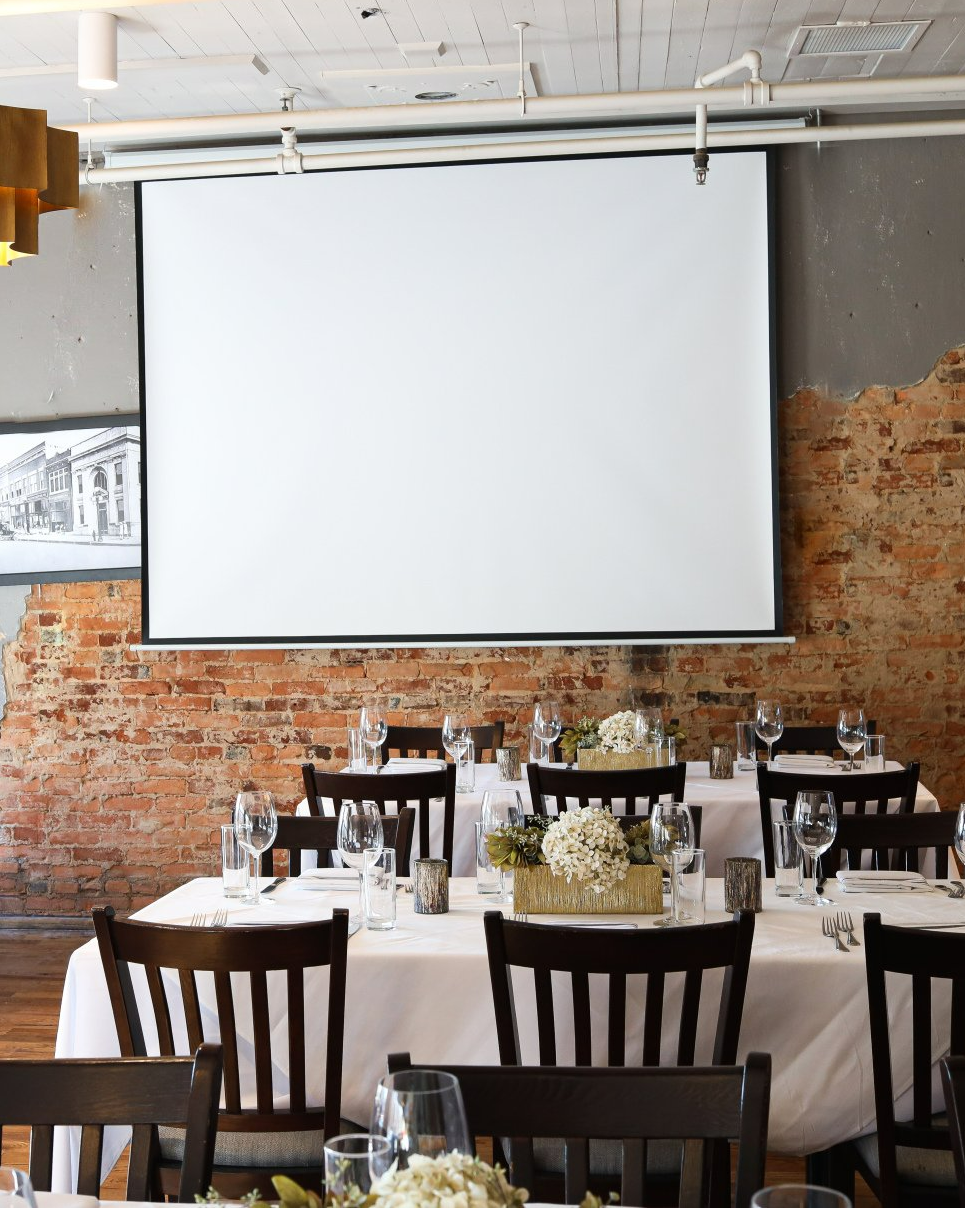 A restaurant with tables and chairs and a projector screen