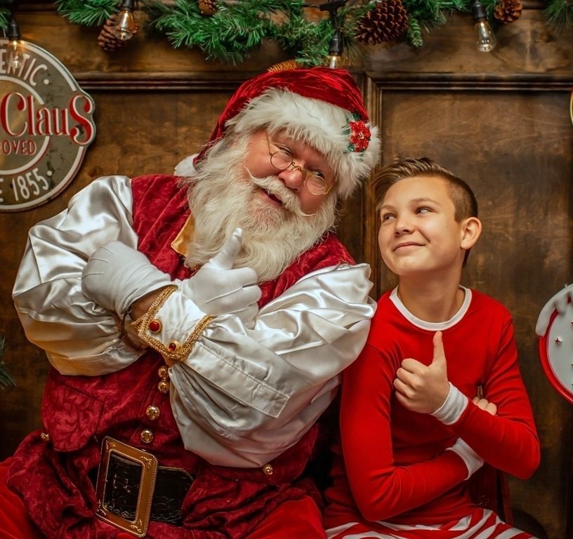 A boy is giving a thumbs up next to a man dressed as santa claus