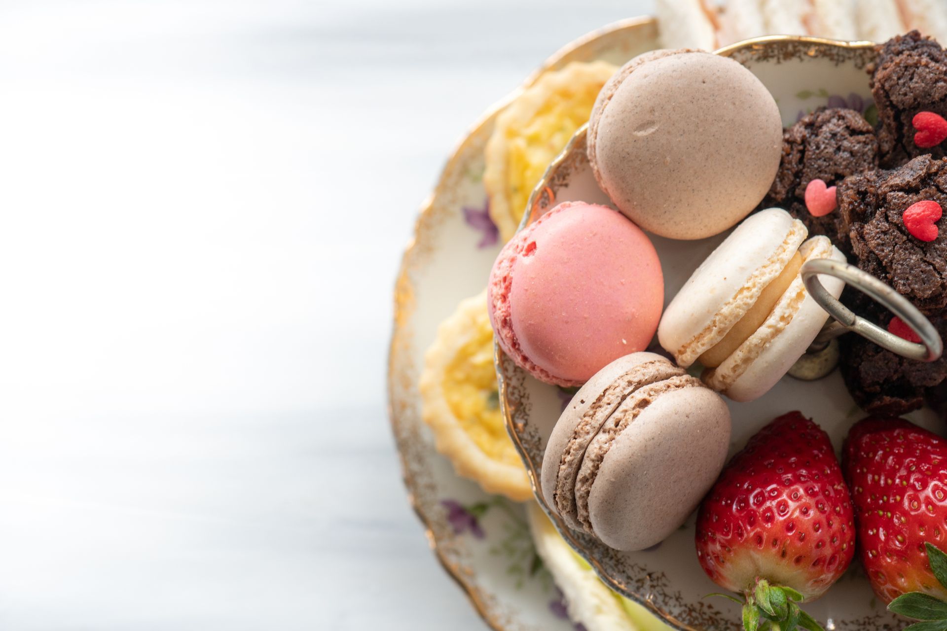 A plate of macarons , strawberries and brownies on a table.