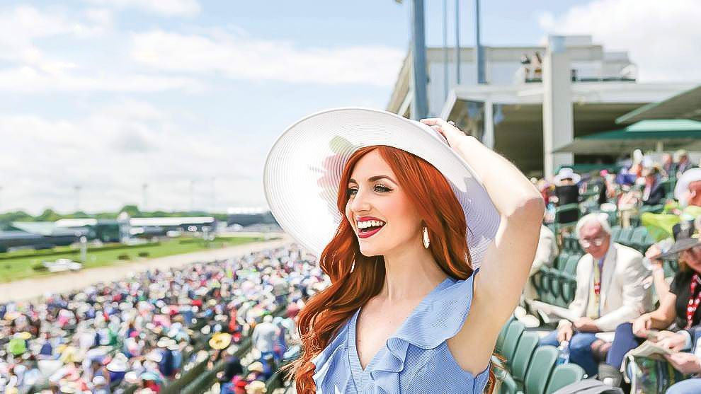 A woman wearing a white hat is standing in front of a crowd at a race track.