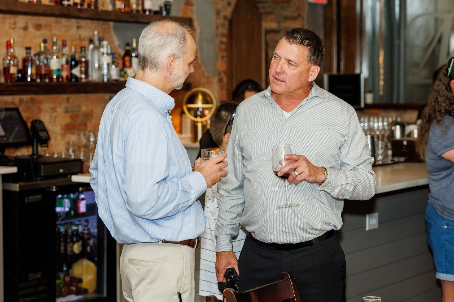 Two men are standing next to each other in a bar talking to each other.