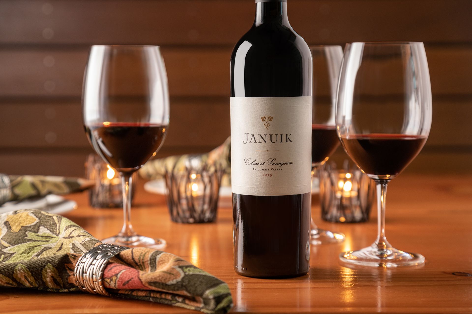 A bottle of wine is sitting on a wooden table next to two glasses of wine.