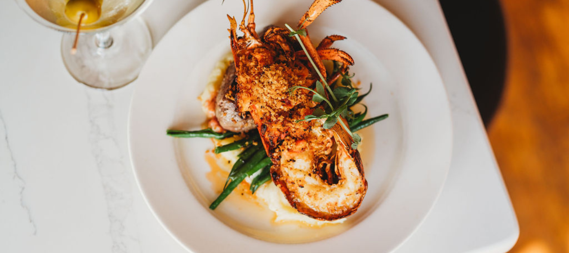A white plate topped with a lobster and green beans next to a martini glass.