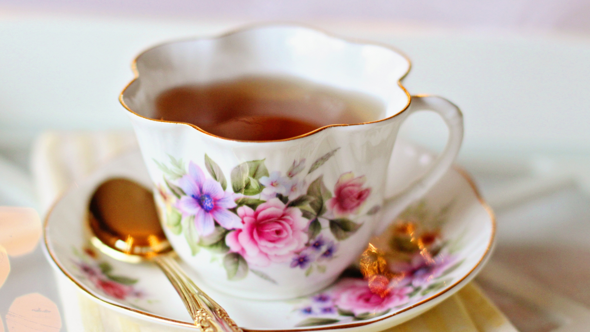 A cup of tea is on a saucer with a gold spoon.