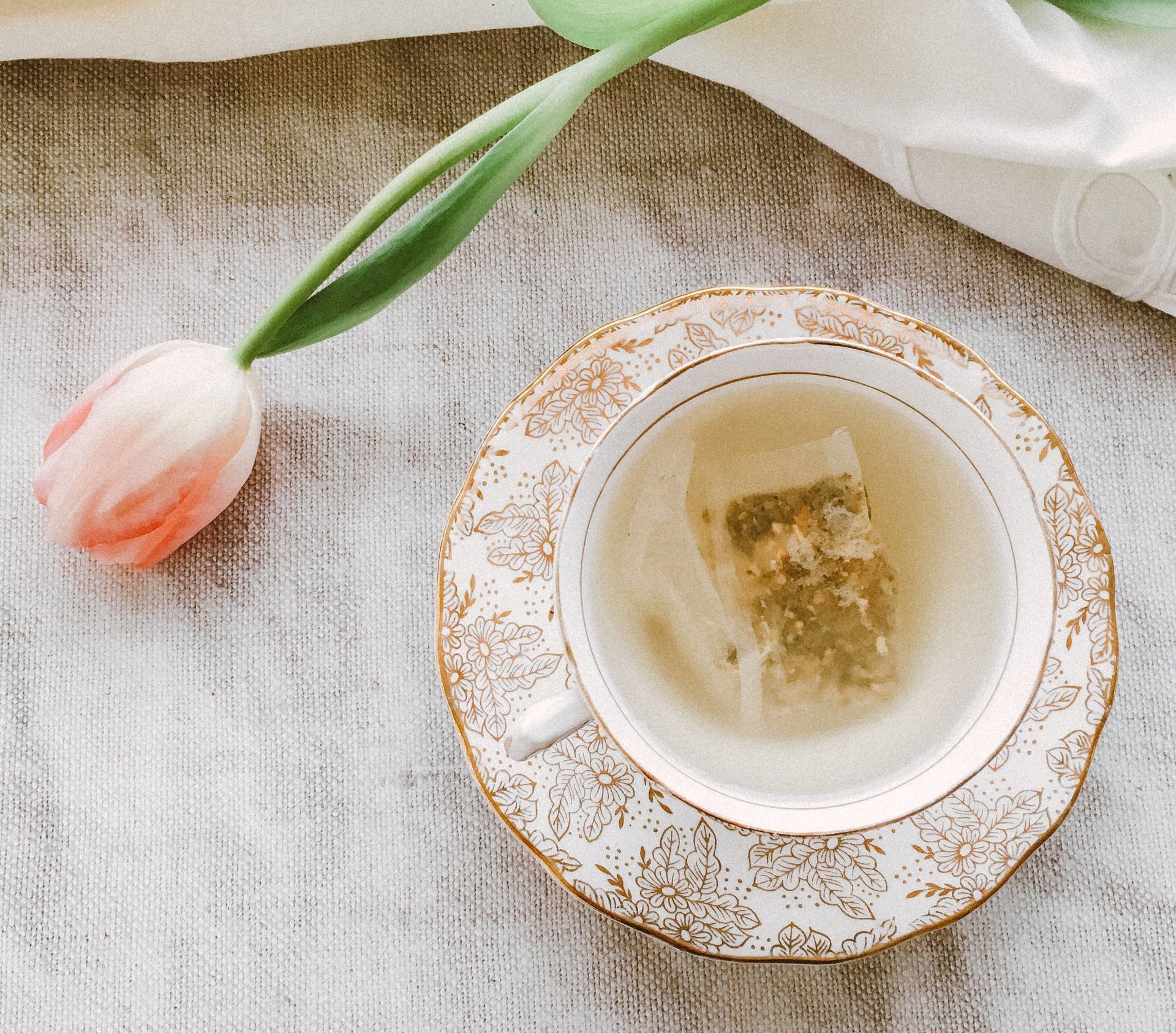 A cup of tea is on a saucer next to a tulip.