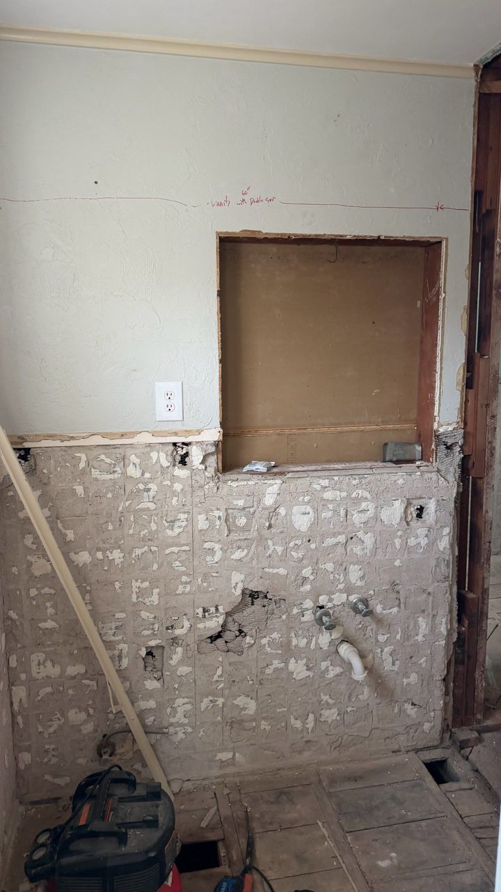 Damaged interior wall with exposed plaster, a small open wall recess, and renovation tools on the floor.