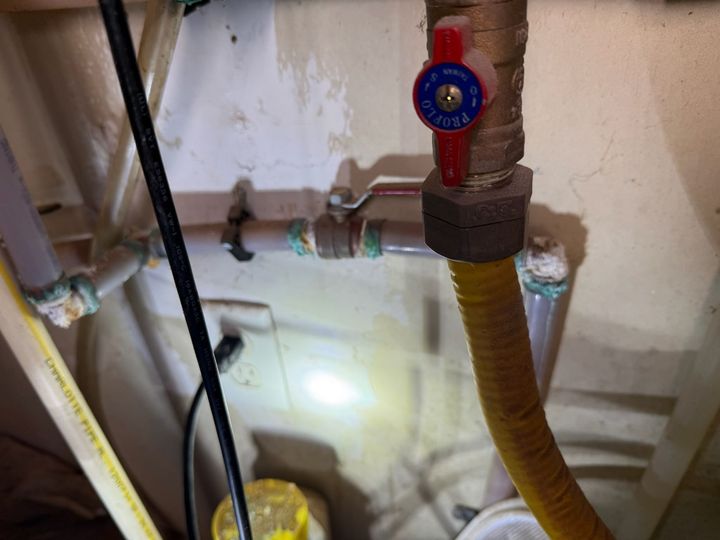 Plumbing pipes with a red valve and yellow hose in a cramped utility space