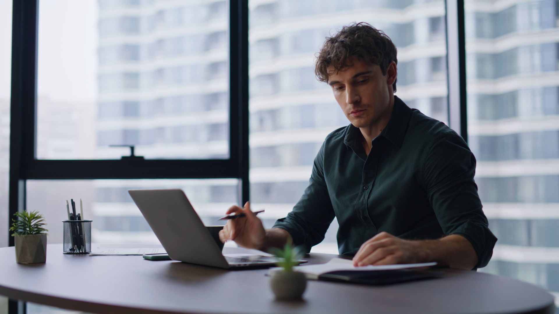Person working at a desk with a laptop and notebook in a bright office.