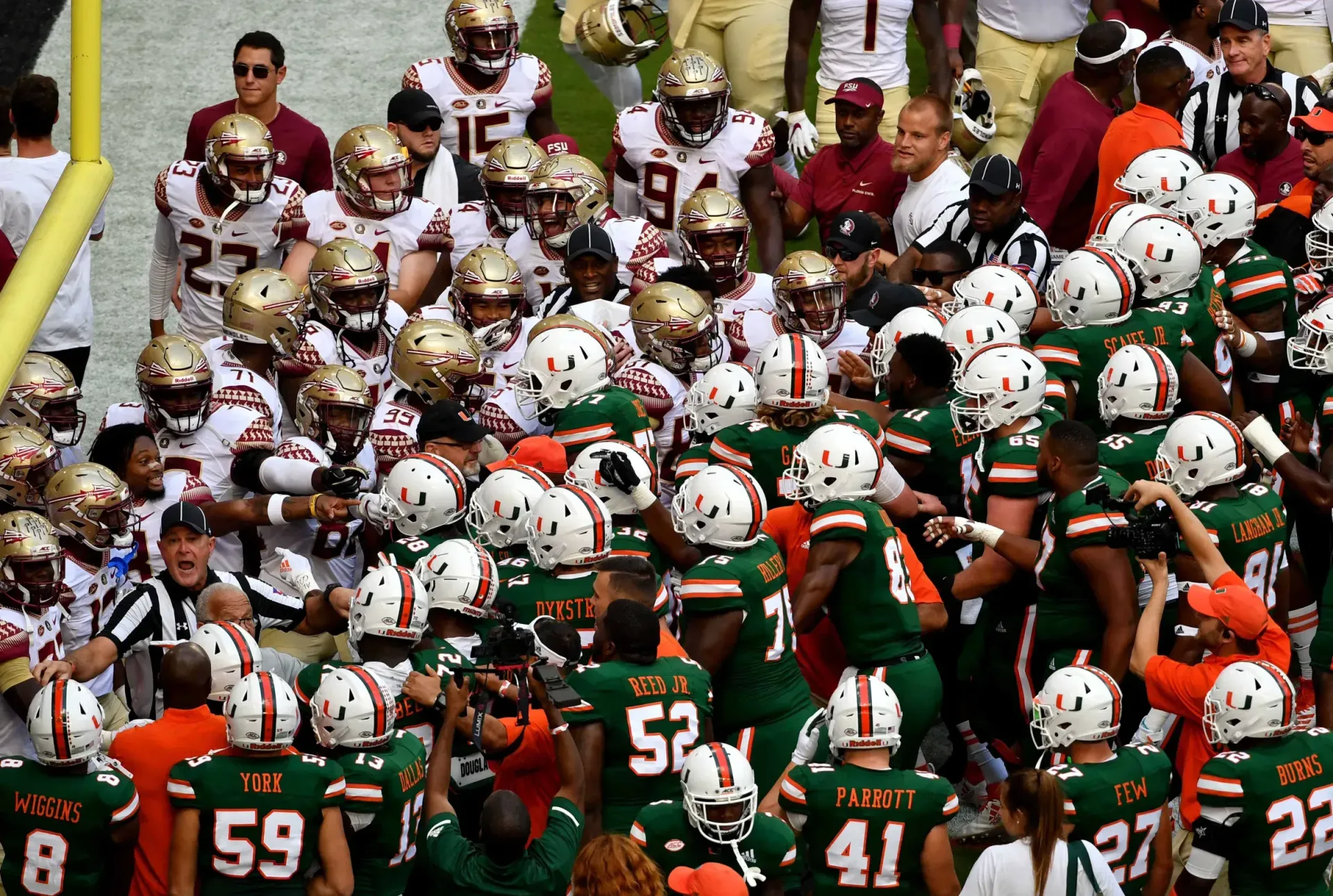 Football teams in green and gold uniforms, maroon and gold uniforms face off on the field.