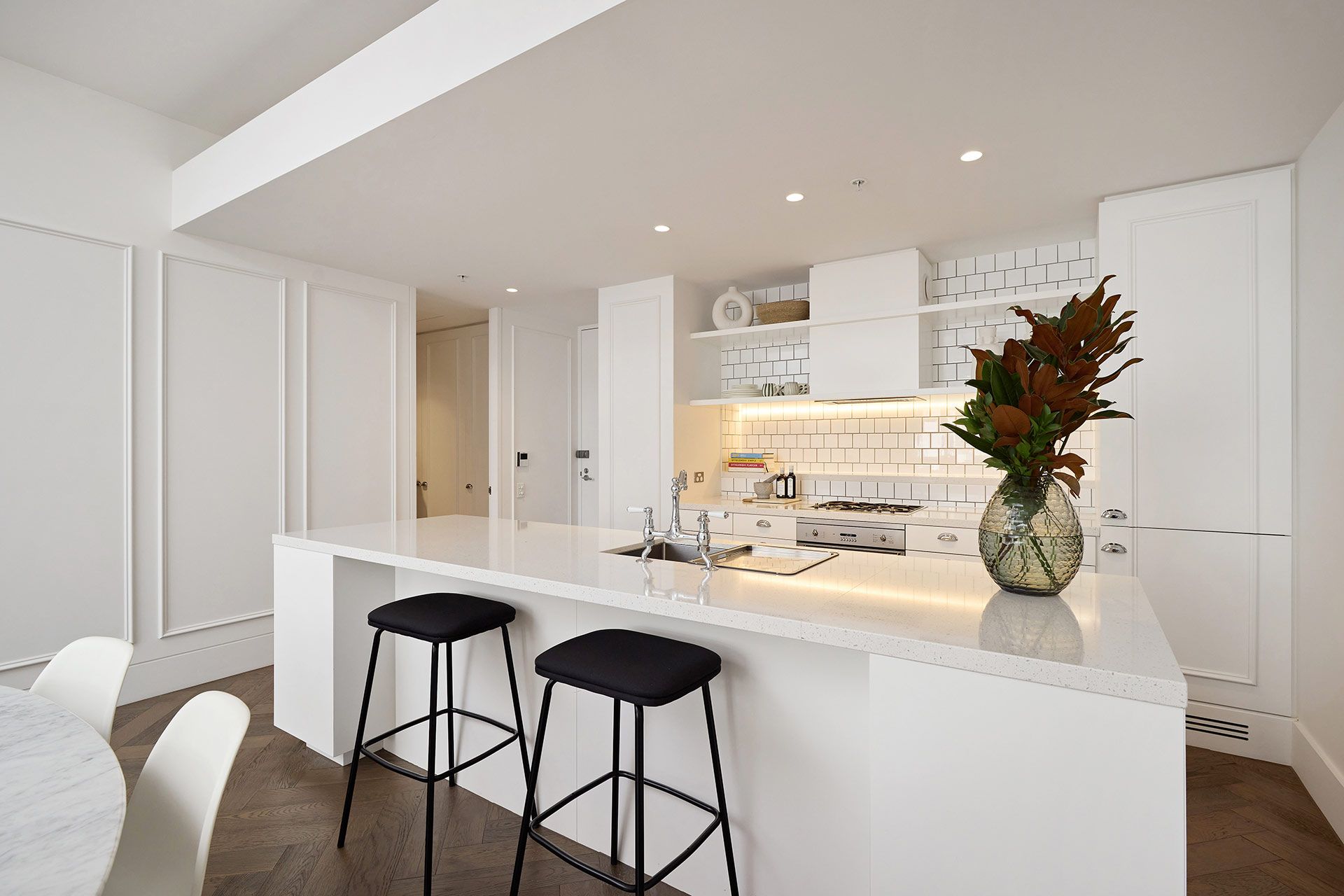 A kitchen with white cabinets and stools and a vase of flowers on the counter.