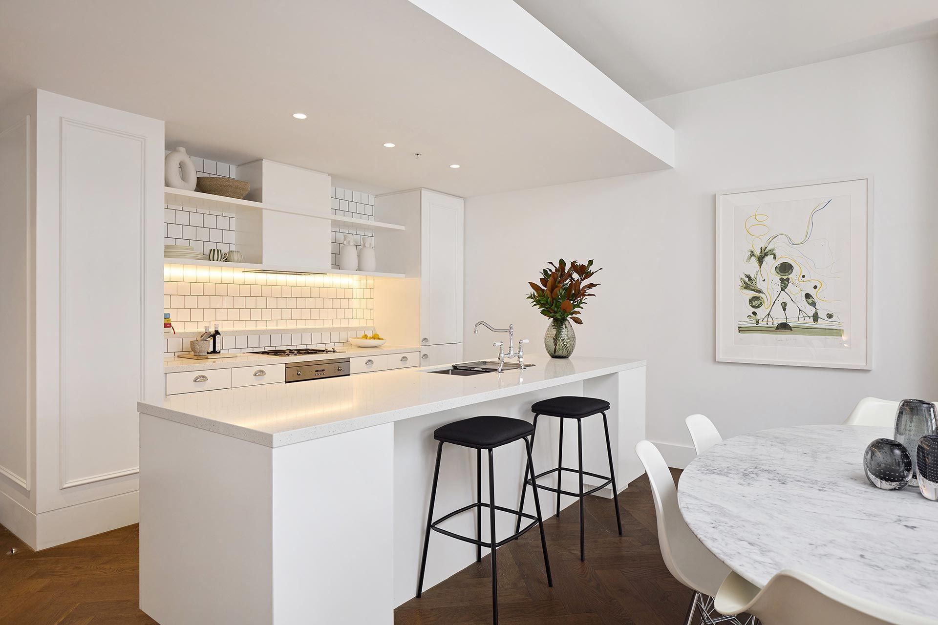 A kitchen with a table and stools and a vase of flowers on the counter.