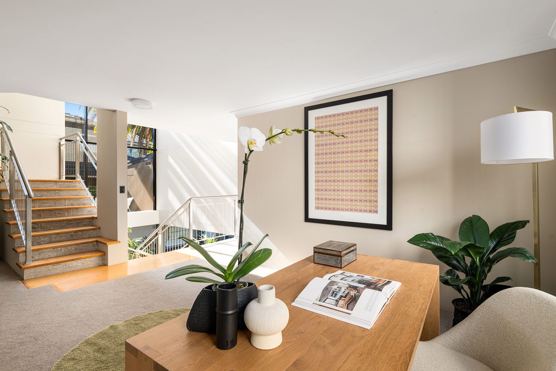 A living room with a coffee table , chair , lamp and stairs.