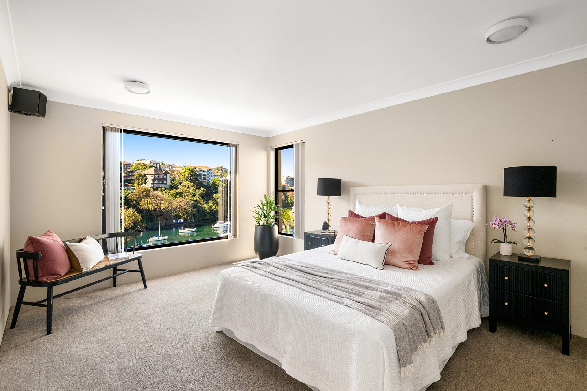 A bedroom with a large bed , nightstand , bench and window.