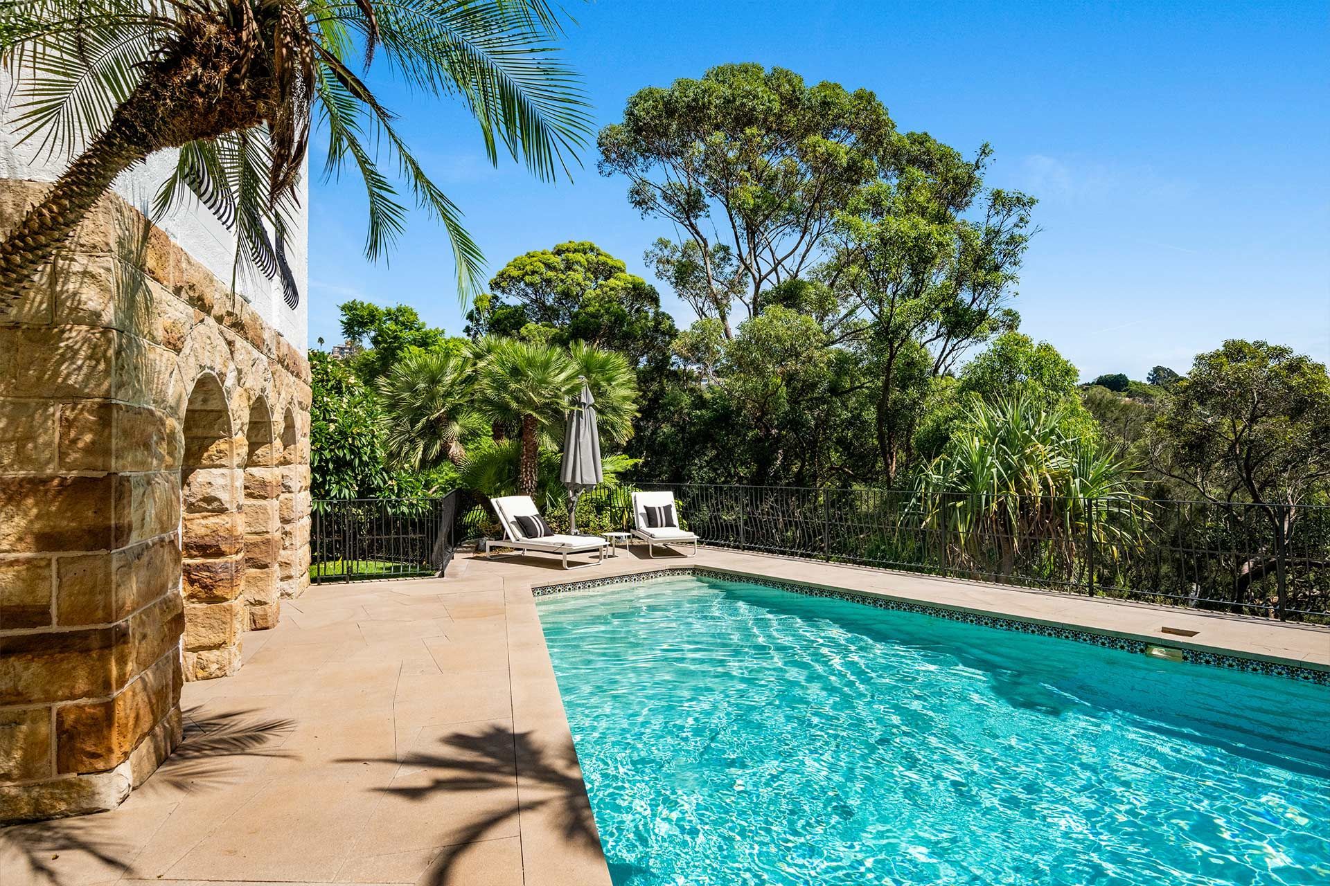 A large swimming pool surrounded by trees and a stone wall.