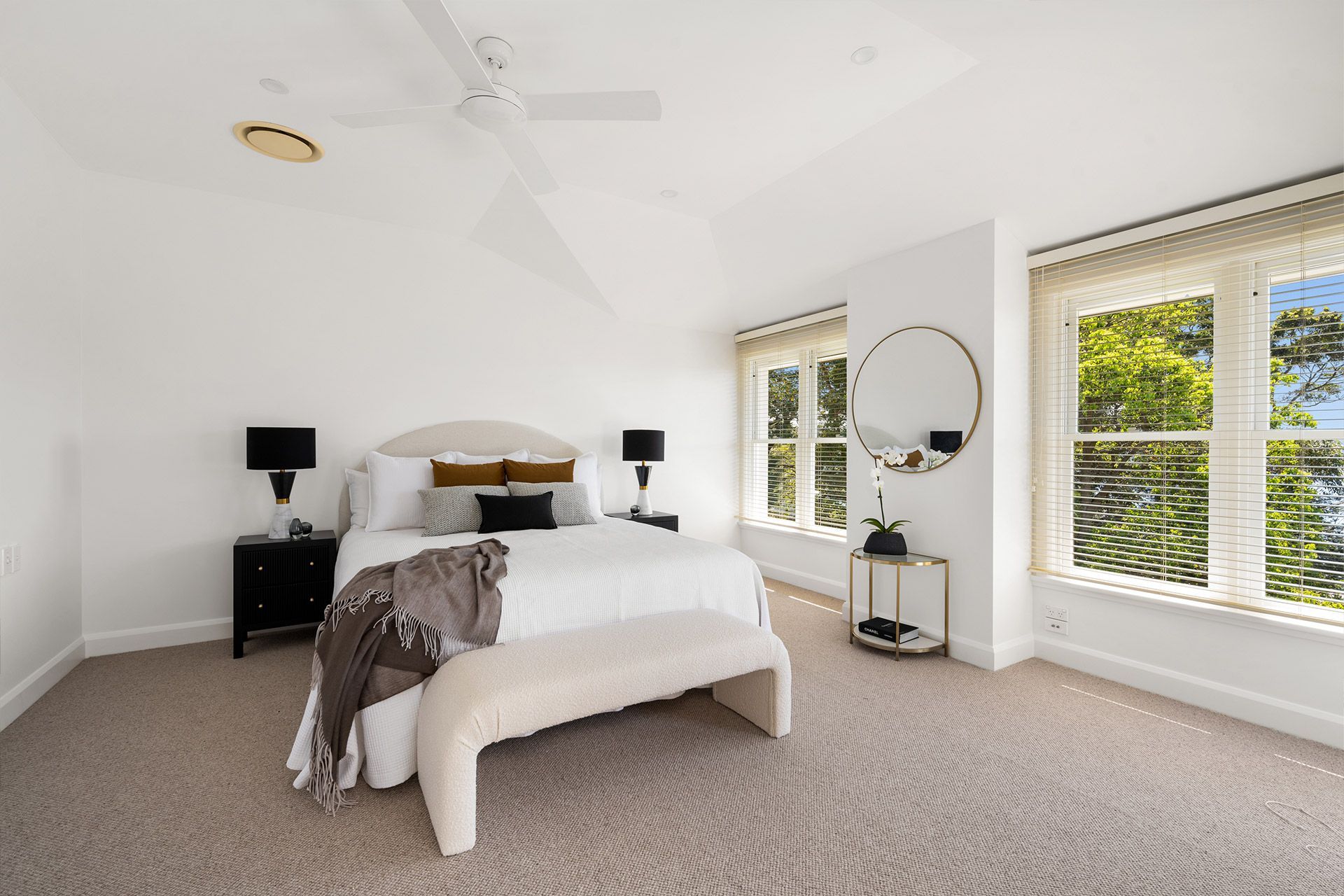 A bedroom with a large bed , a bench , a mirror and a ceiling fan.
