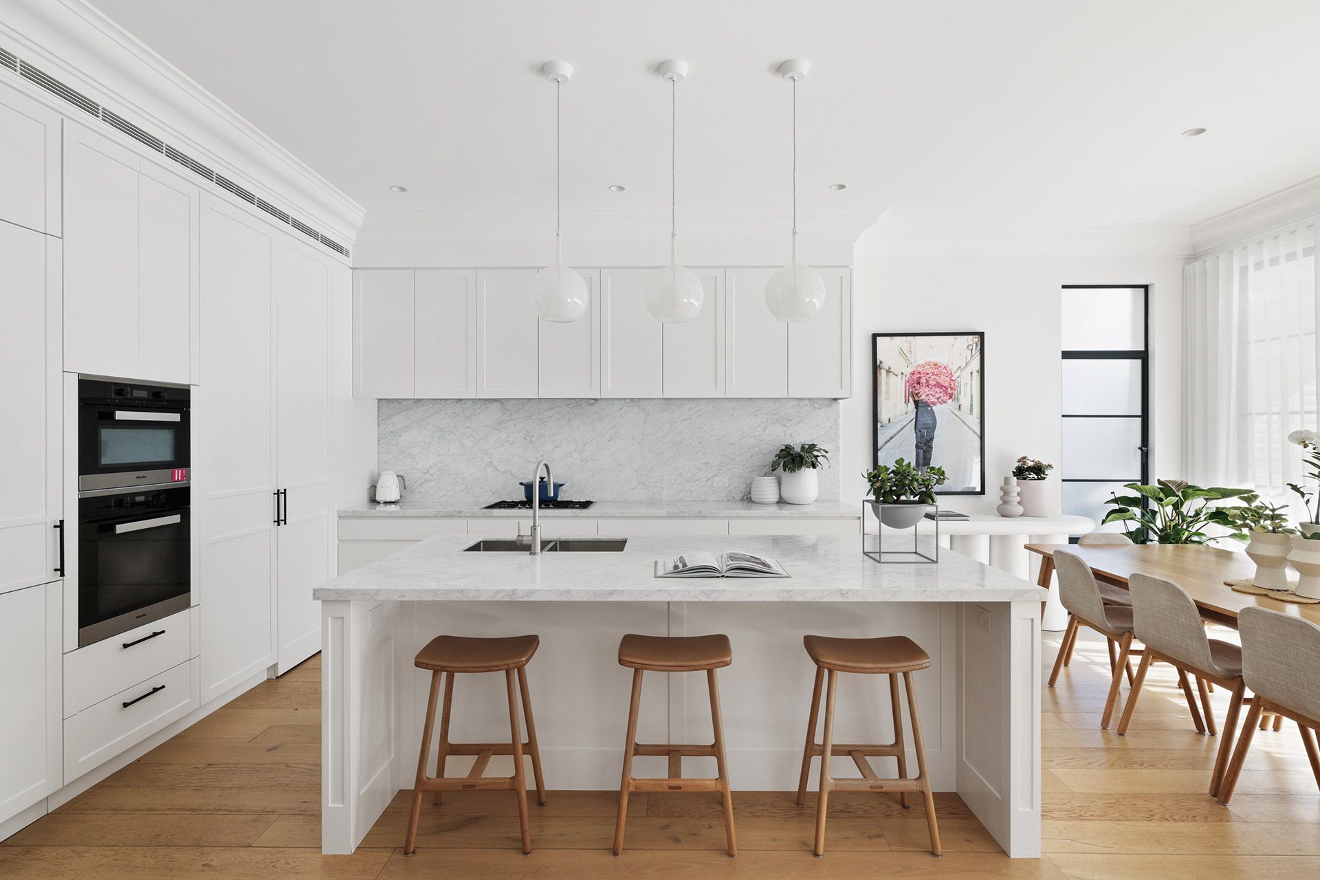 A kitchen with white cabinets , wooden floors , stools and a large island. Beauty Point.