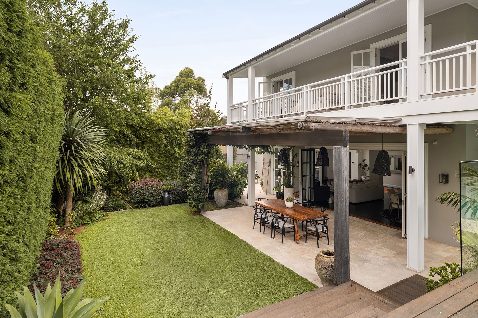 A large house with a large lawn and a patio with a table and chairs.