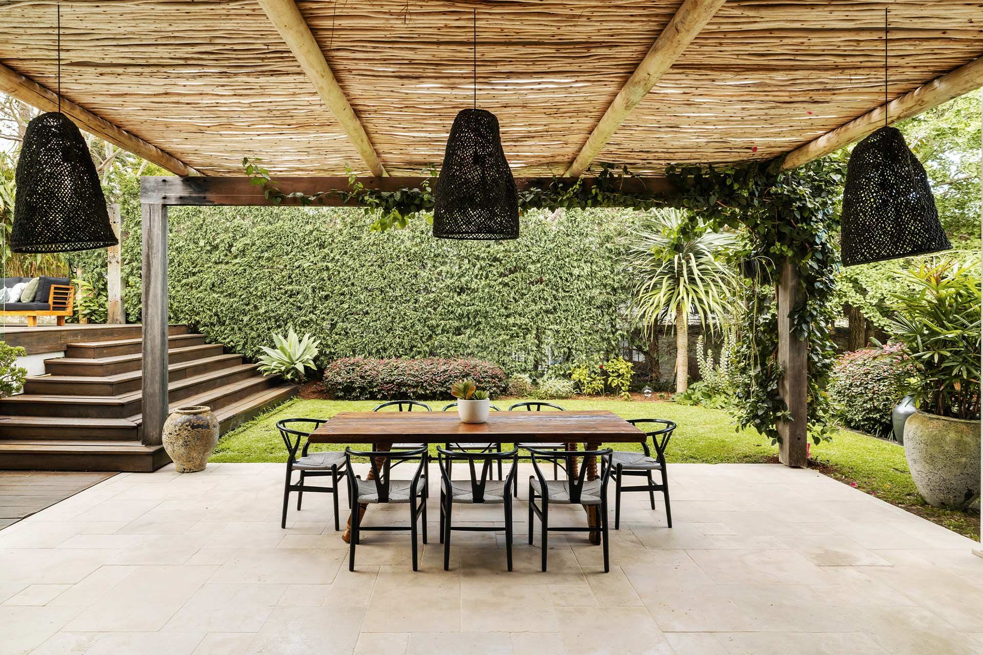 There is a table and chairs under a wooden pergola.