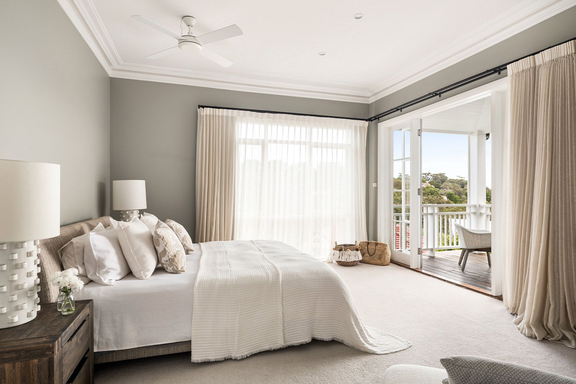 A bedroom with a bed , lamps , curtains and a ceiling fan.