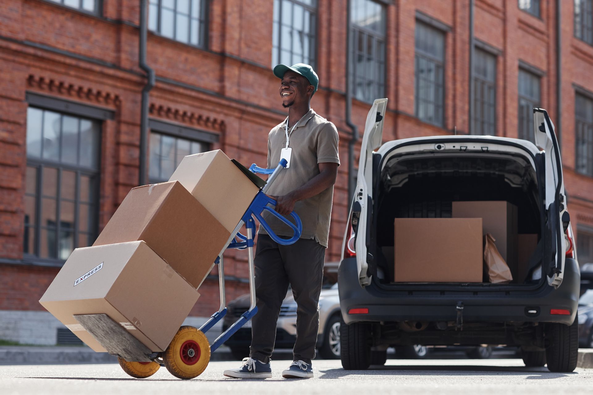 A delivery man is pushing a cart full of boxes next to a van.