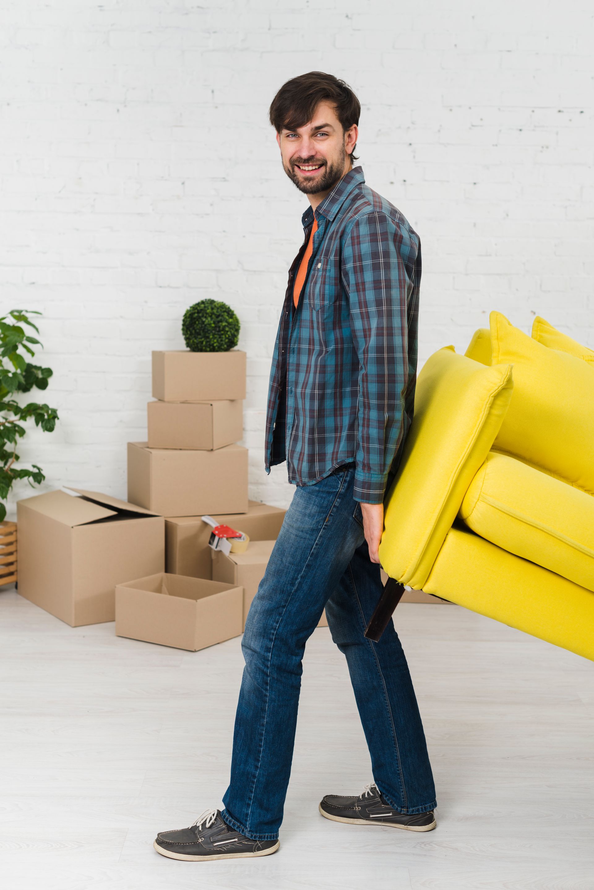 A man is carrying a yellow couch in a living room.