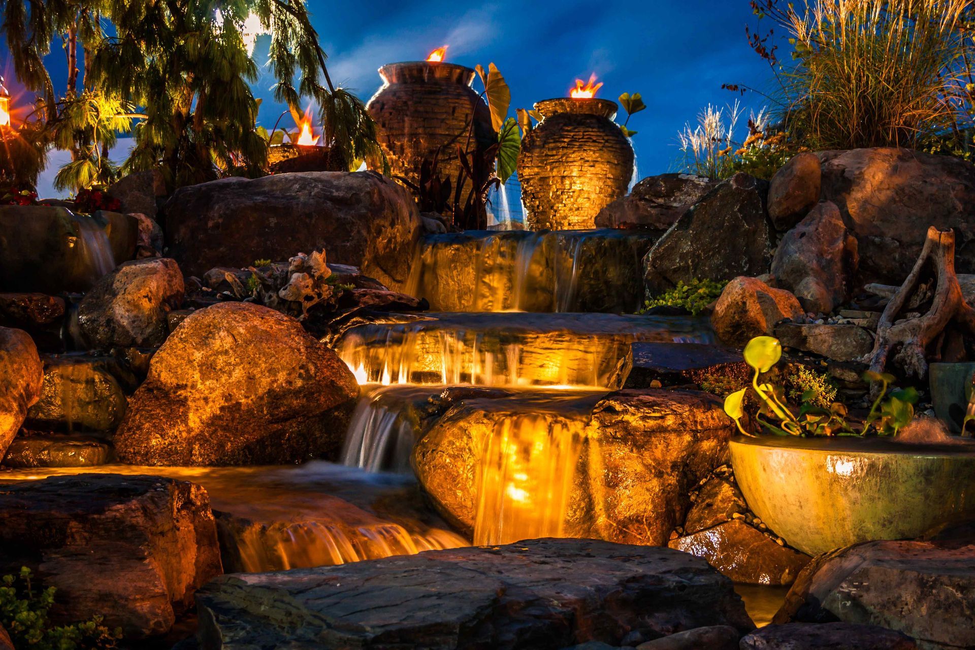 night-time water fall down lit-up boulders, shrubs, and vase theming