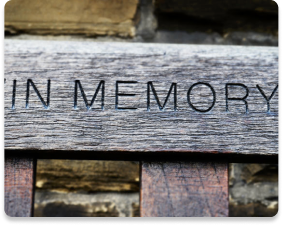 Weathered wooden plaque engraved “IN MEMORY” against a stone wall