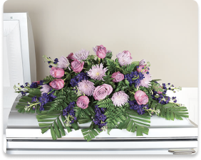 Purple and pink floral arrangement on a white coffin, with green fern leaves