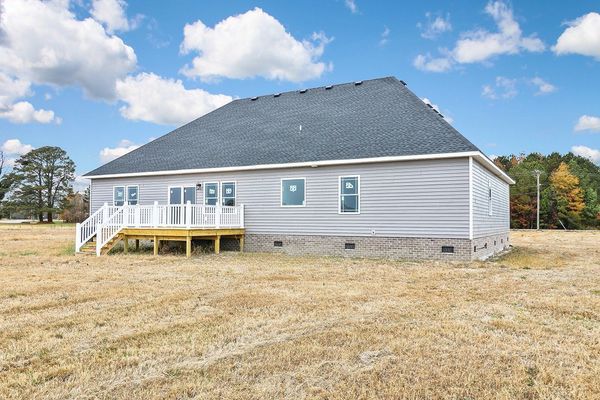 Back view of a light gray house with a small white deck on a brown field under a cloudy sky.