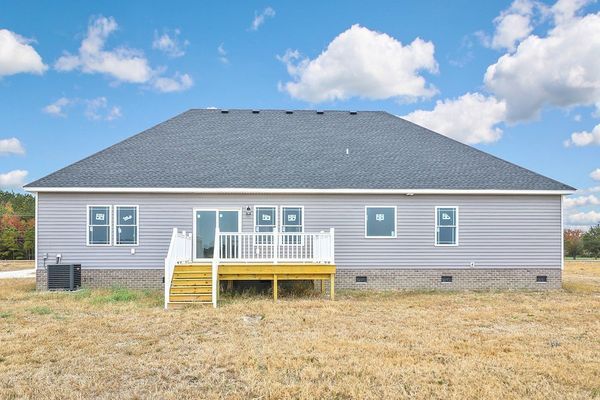 Back of a single-story house with gray siding, a deck, and a blue sky with clouds.