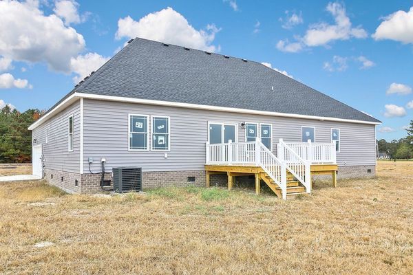 Rear view of a light gray house with a deck and stairs, set in a grassy field with a blue sky.