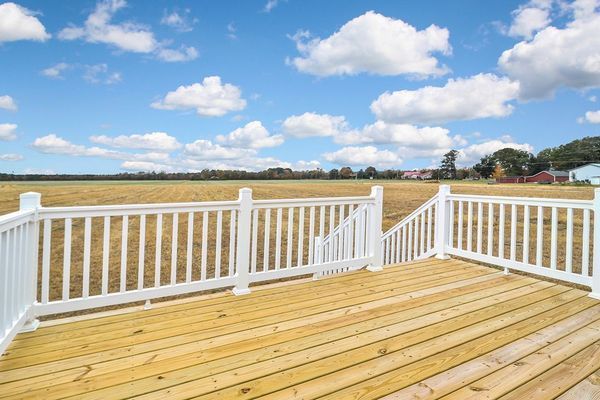 Wooden deck with white railing overlooking a field under a blue sky with clouds.