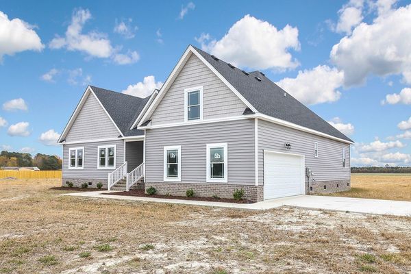 Gray house with white trim, a single-car garage, and a blue sky with clouds in a field.