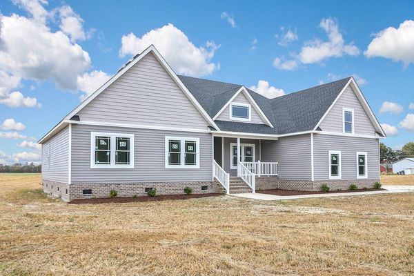 Gray house with white trim, sitting on a grassy lot under a partly cloudy sky.