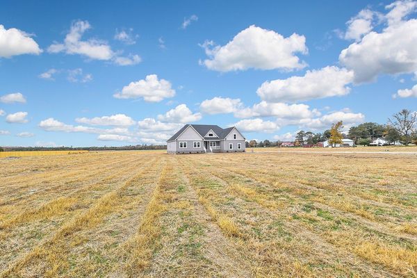 A house sits in a vast field under a blue sky with clouds.