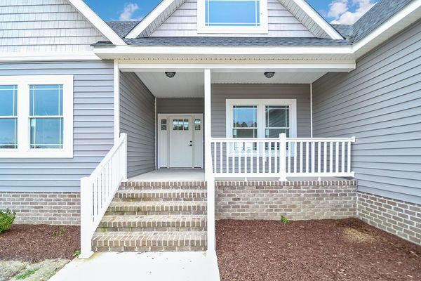 A house with a gray exterior, white trim, and a brick-based porch, leading to a front door.