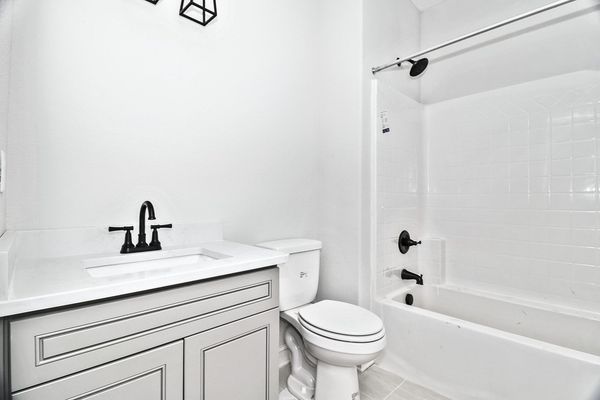 White bathroom with gray vanity, black fixtures, and a toilet.