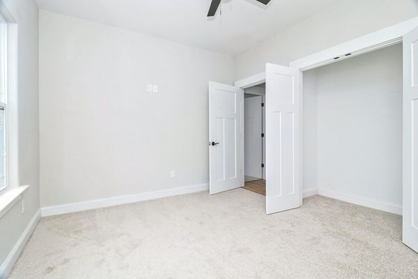 Empty, light-colored bedroom with beige carpet, white walls, and open closet doors.