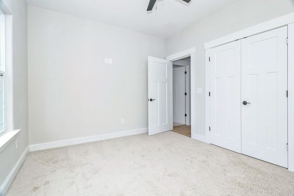 Empty bedroom with white walls, carpet, closet, and a partially open door.